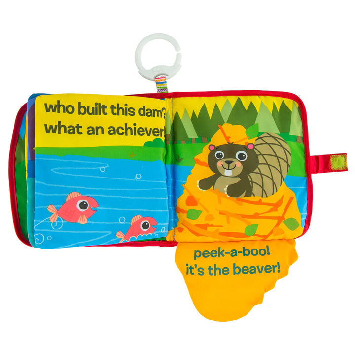 A colorful fabric baby book with a white hanging loop. The book shows a beaver wrapped in a yellow blanket on the right page with the text 'peek-a-boo! it's the beaver!', and fish in blue water on the left page with the text 'who built this dam: what an achiever!'.