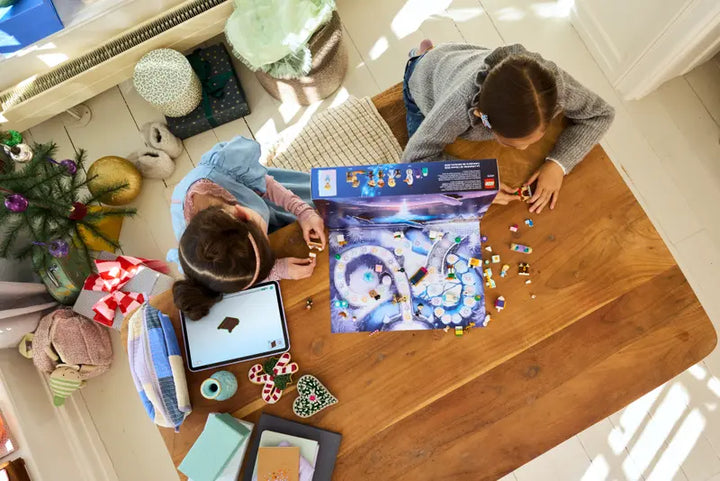 Two children playing with a lego frozen advent calender on a wooden table in a cozy living room.