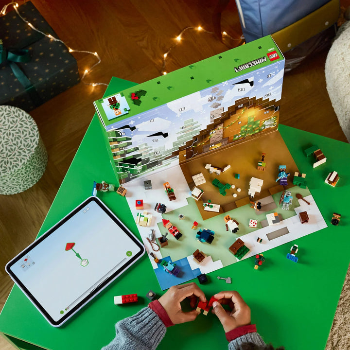 Person building a LEGO Minecraft advent set with a tablet showing the game interface on a green table.