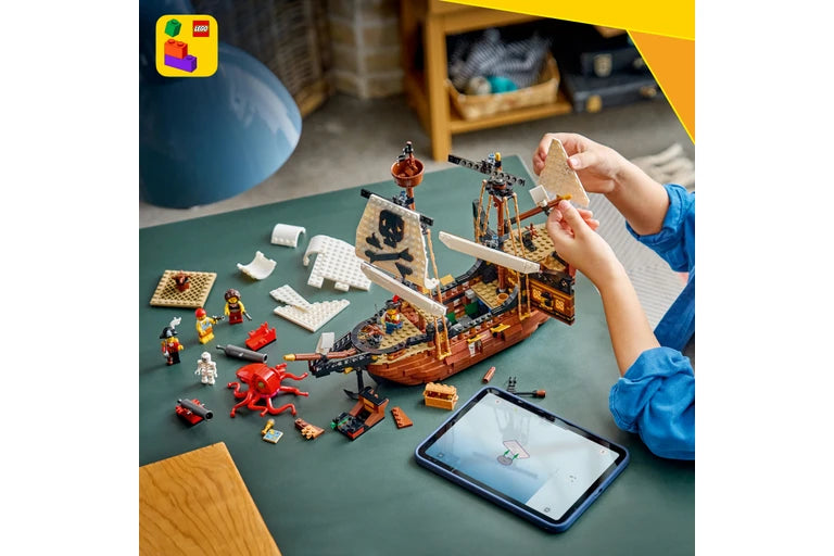 Child playing with a LEGO pirate ship set on a table, using a tablet.
