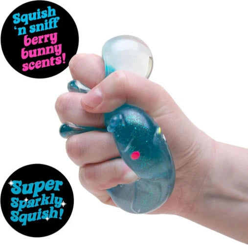 Hand holding a nee doh blue glittery squishy toy with text about berry bunny scents and sparkly texture.