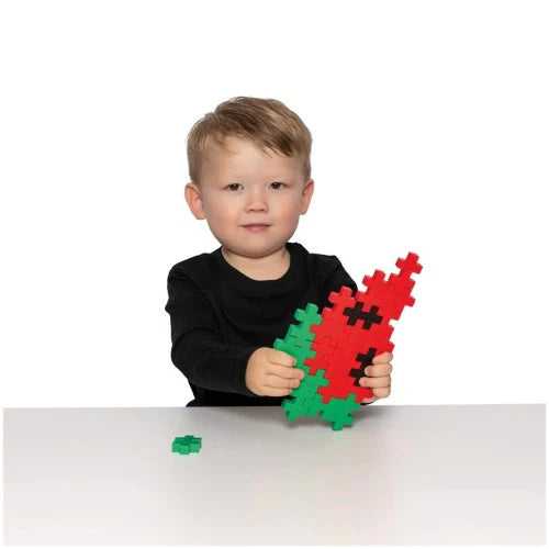 Child holding a red and green plus plus puzzle piece toy on a white background