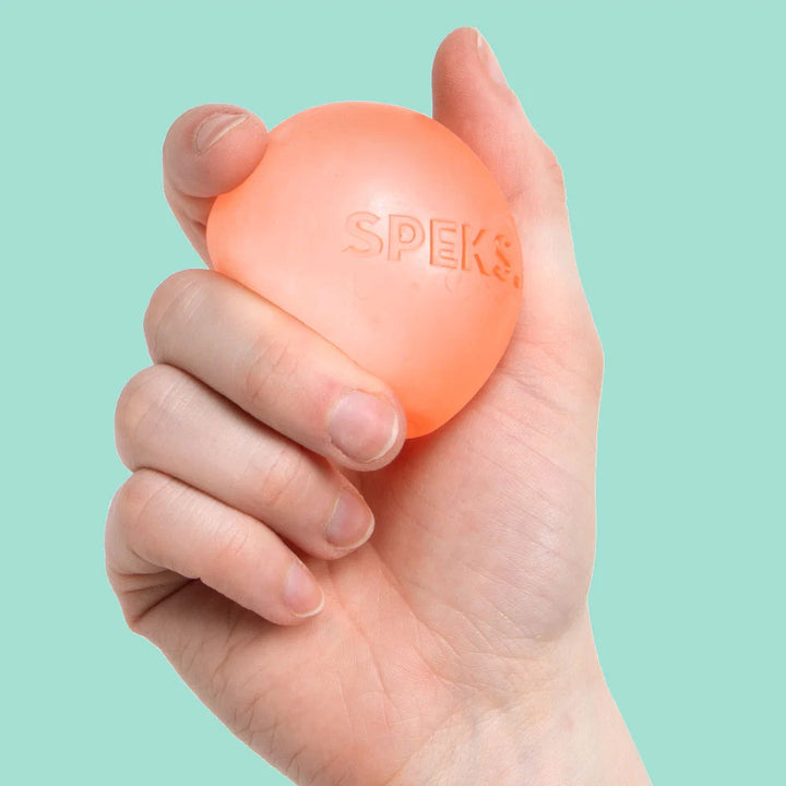 A hand holding a small, reef coloured stress ball with the brand name 'SPEKS' embossed on the front, set against a solid mint green background.