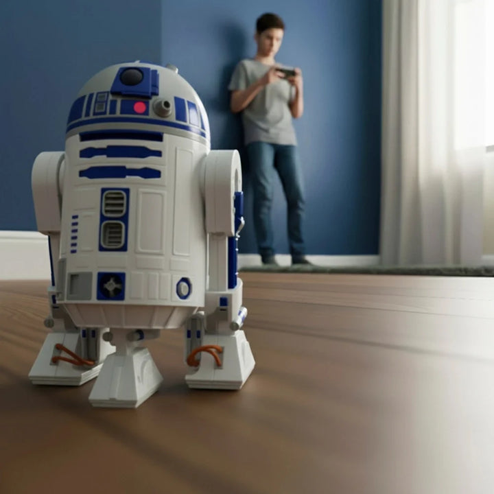 R2-D2 toy being controlled by a boy in the background of image inside a room