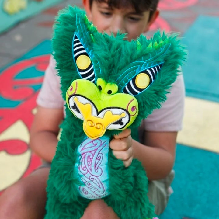 Child holding a green taniwha toy with colorful design