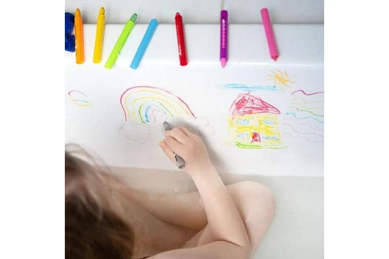 Child drawing a rainbow with crayons on a white sheet of paper.