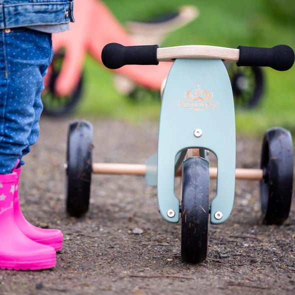 Children's balance bike with a child in pink boots standing next to it on a path.
