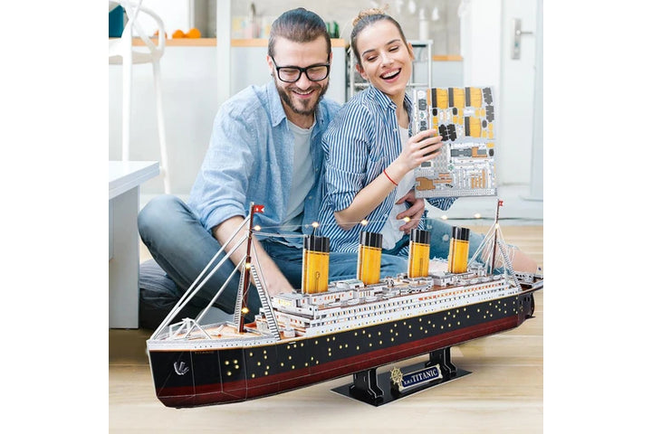 Two people with a large titanic cubic fun model ship indoors