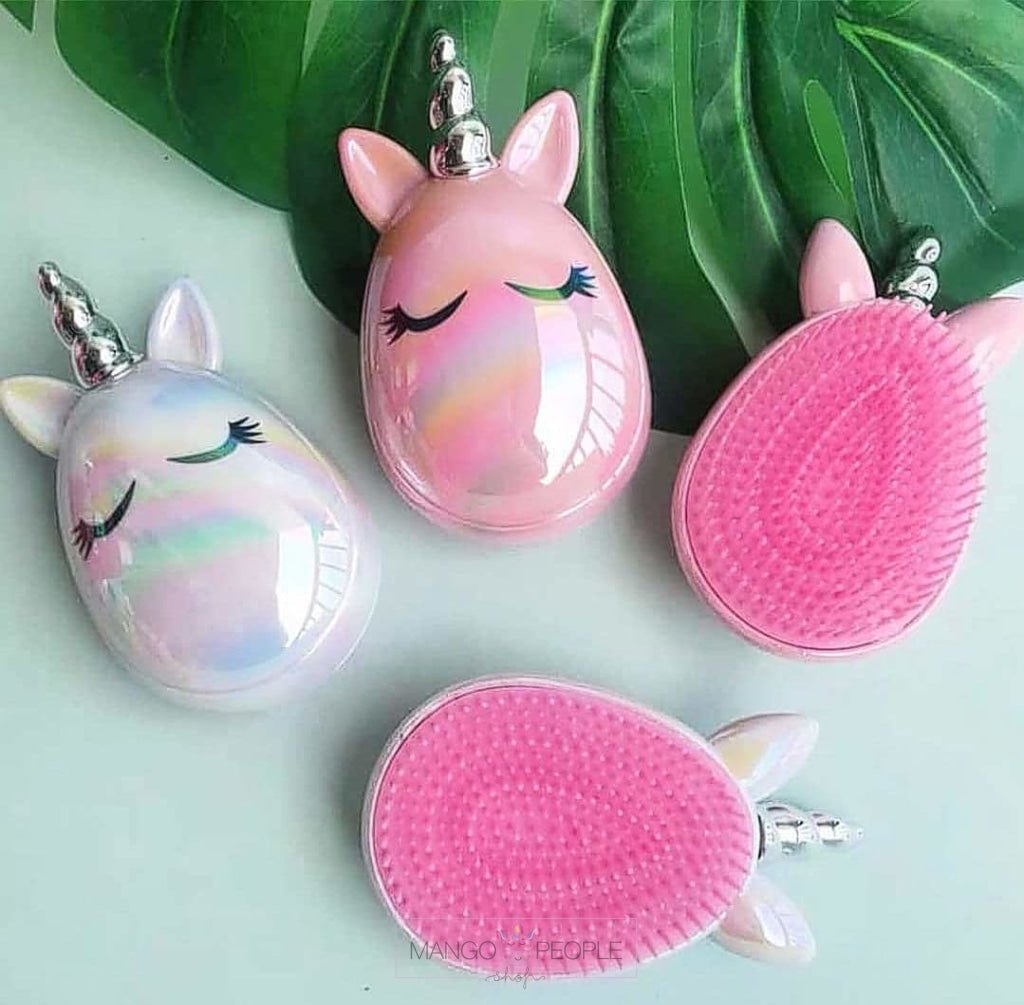 Three small unicorn-shaped hairbrushes arranged on a pale mint background with large green leaves. One brush is shown from the front with a glossy iridescent white body, closed eyes, and silver horn; another shows the pink bristle side; the third is angled to show both sides.