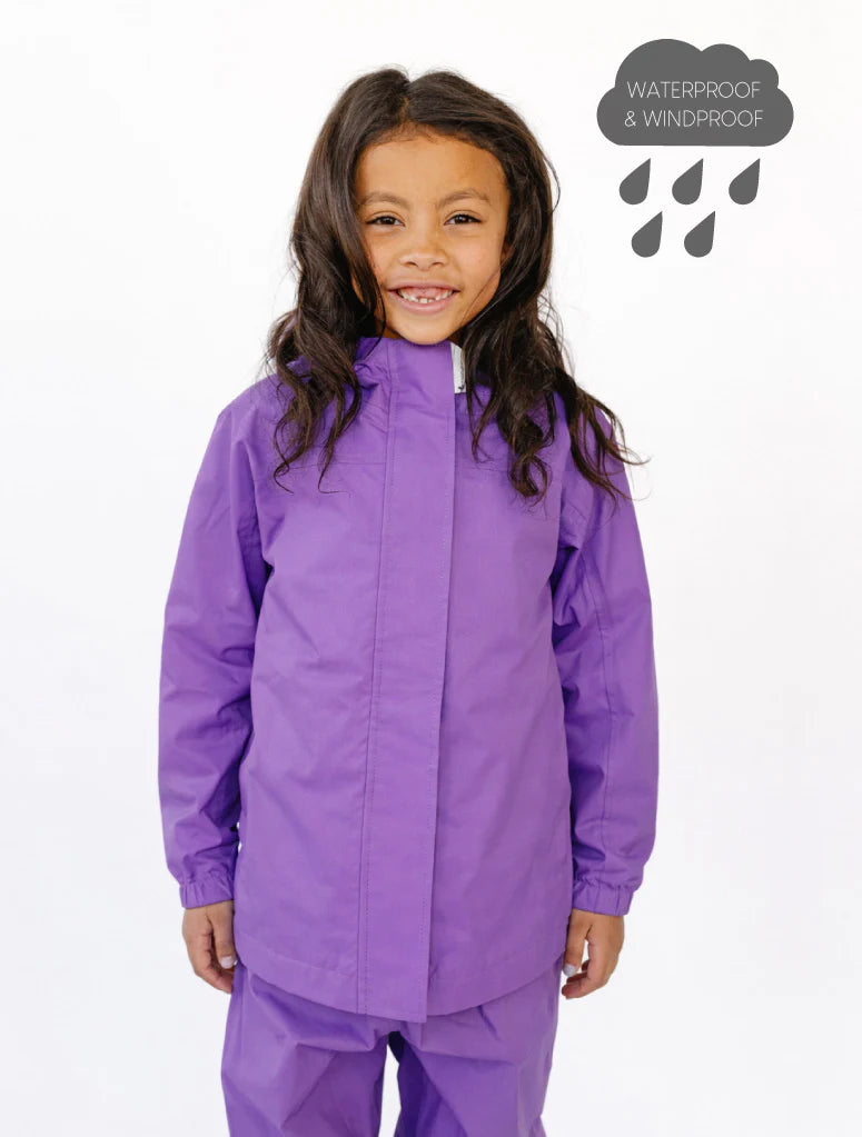 Child wearing a purple waterproof jacket and pants on a white background