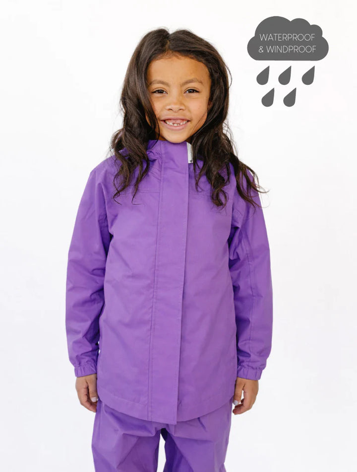 Child wearing a purple waterproof jacket and pants on a white background