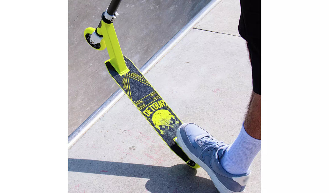 Person riding a scooter with 'Detour' branding on a sidewalk.